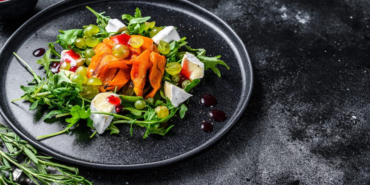 Autumn salad with baked pumpkin and brie cheese. Healthy vegan food concept. Black background